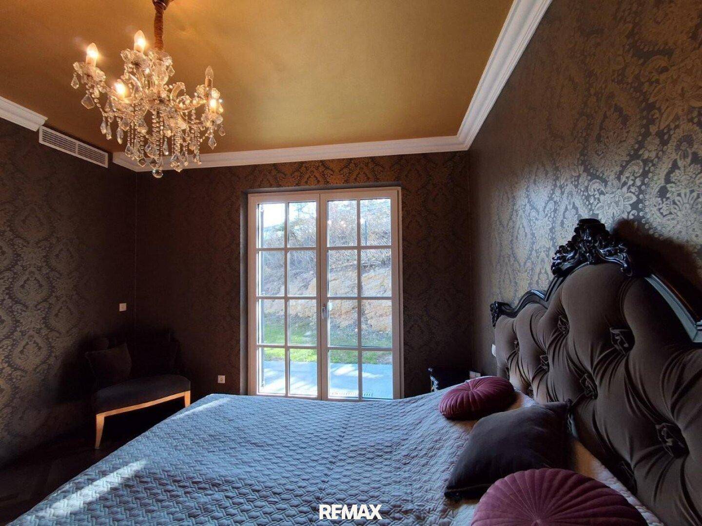 Elegantes Schlafzimmer mit dunkler Tapete, Kronleuchter und Zugang zum Außenbereich.