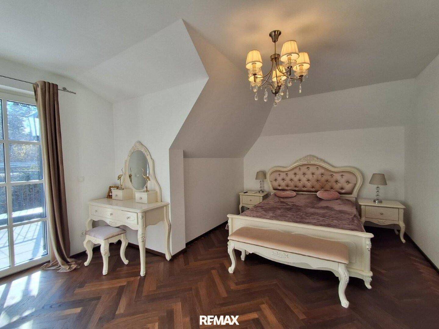 Elegantes Schlafzimmer mit Holzboden, Schminktisch und Zugang zum Balkon.