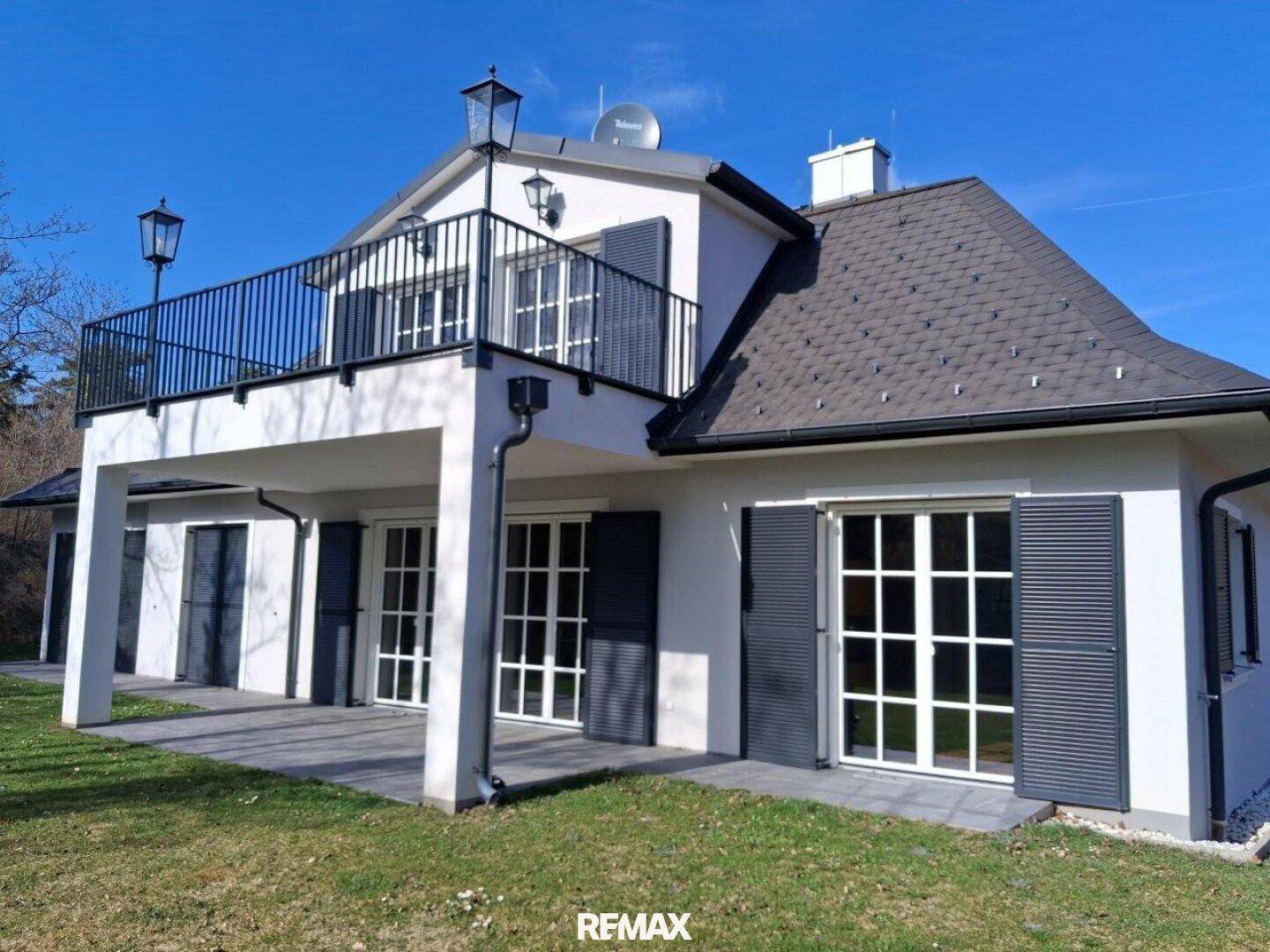 Rückseite des Hauses mit großem Balkon, Terrasse und Zugang zum Garten durch breite Fenster.