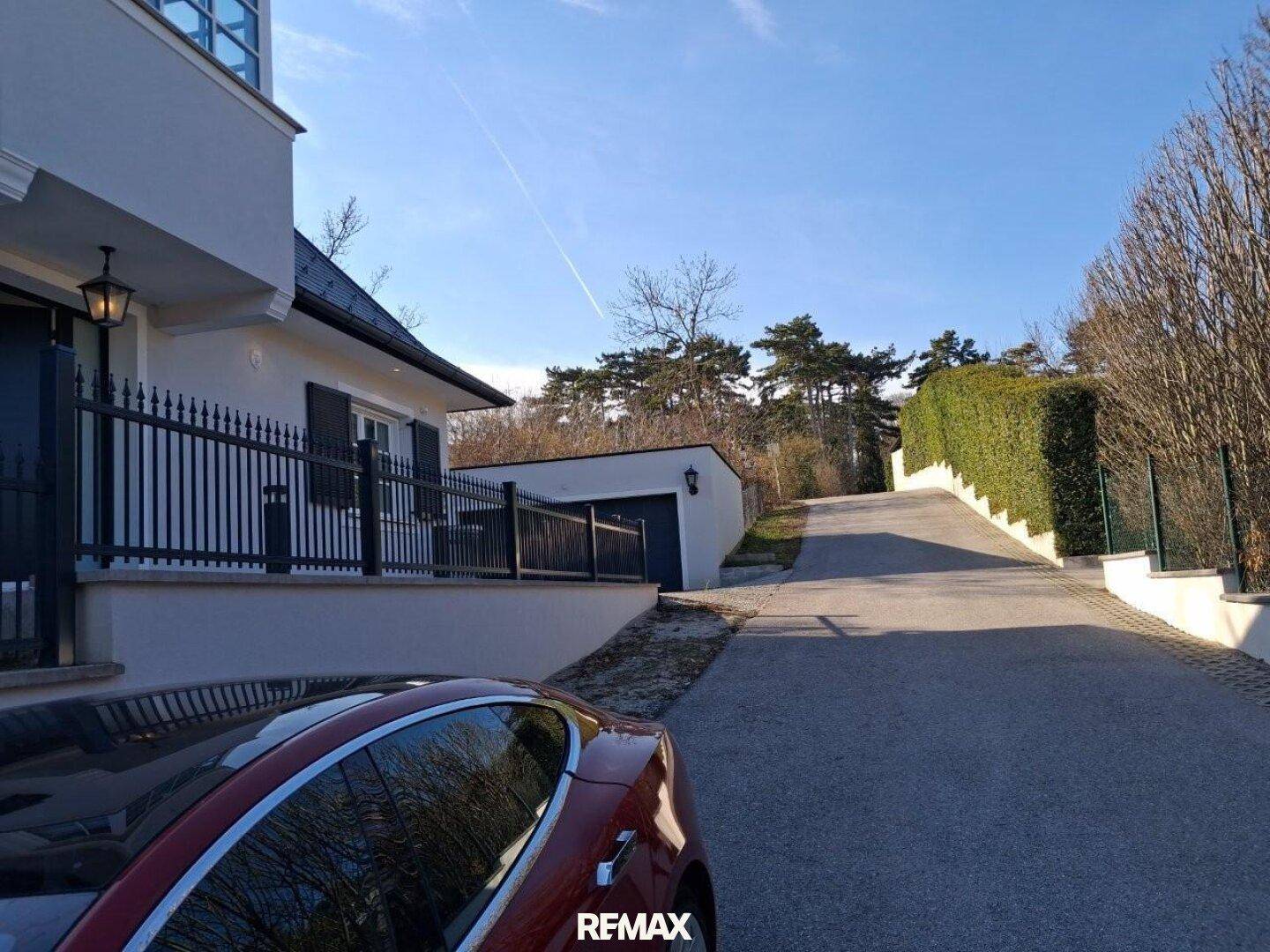 Zufahrt zum Haus mit gepflegter Hecke und Bäumen im Hintergrund, die eine grüne Aussicht bieten.