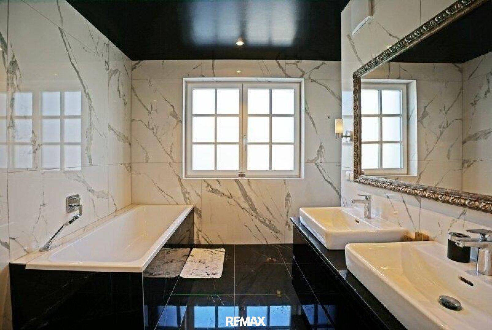 Luxuriöses Badezimmer mit Marmorfliesen, Doppelwaschbecken, Badewanne und großem Spiegel.
