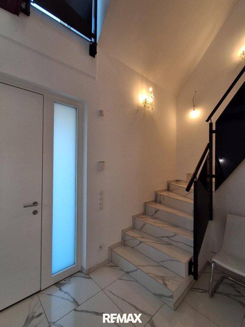 Heller Treppenaufgang mit Marmorfliesen, elegantem Geländer und Wandleuchten.