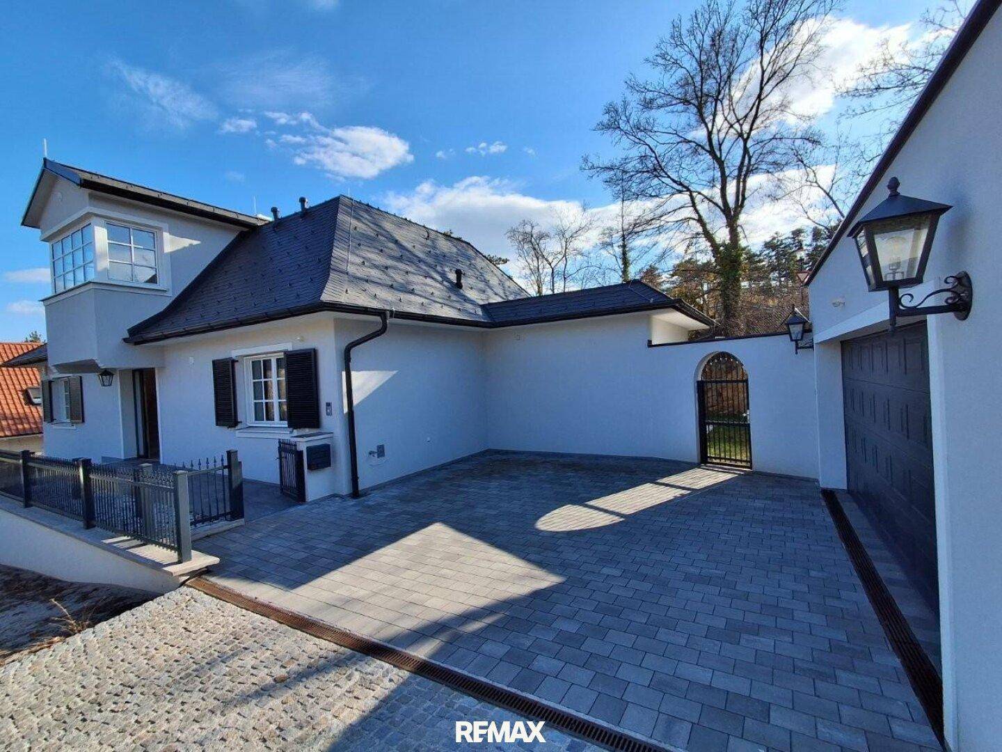 Außenansicht des Hauses mit gepflastertem Vorplatz, integrierter Garage und einem schmiedeeisernen Tor.