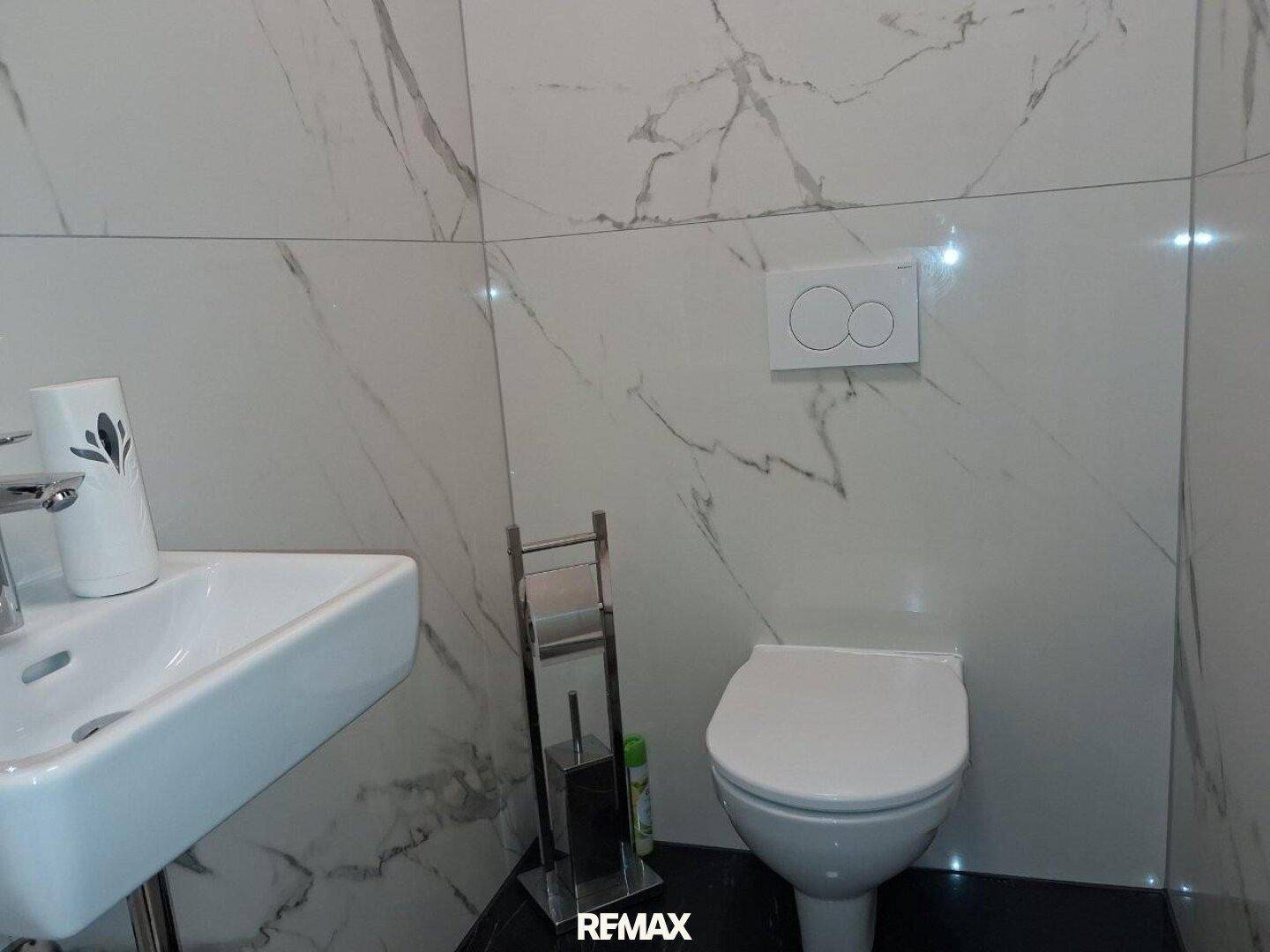 Kleines Gäste-WC mit Marmorfliesen, wandhängendem WC und modernem Waschbecken.
