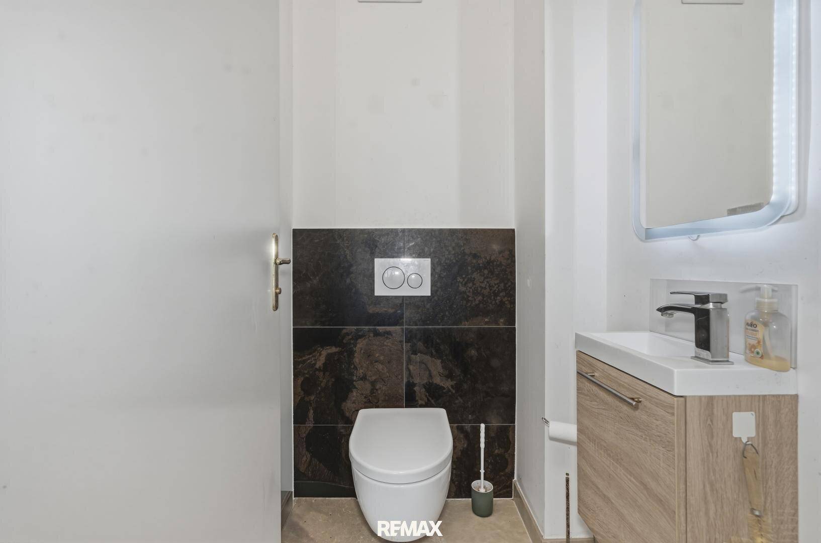 Modernes Gäste-WC mit dunklen Fliesen, wandhängendem WC und stilvollem Einzelwaschbecken.