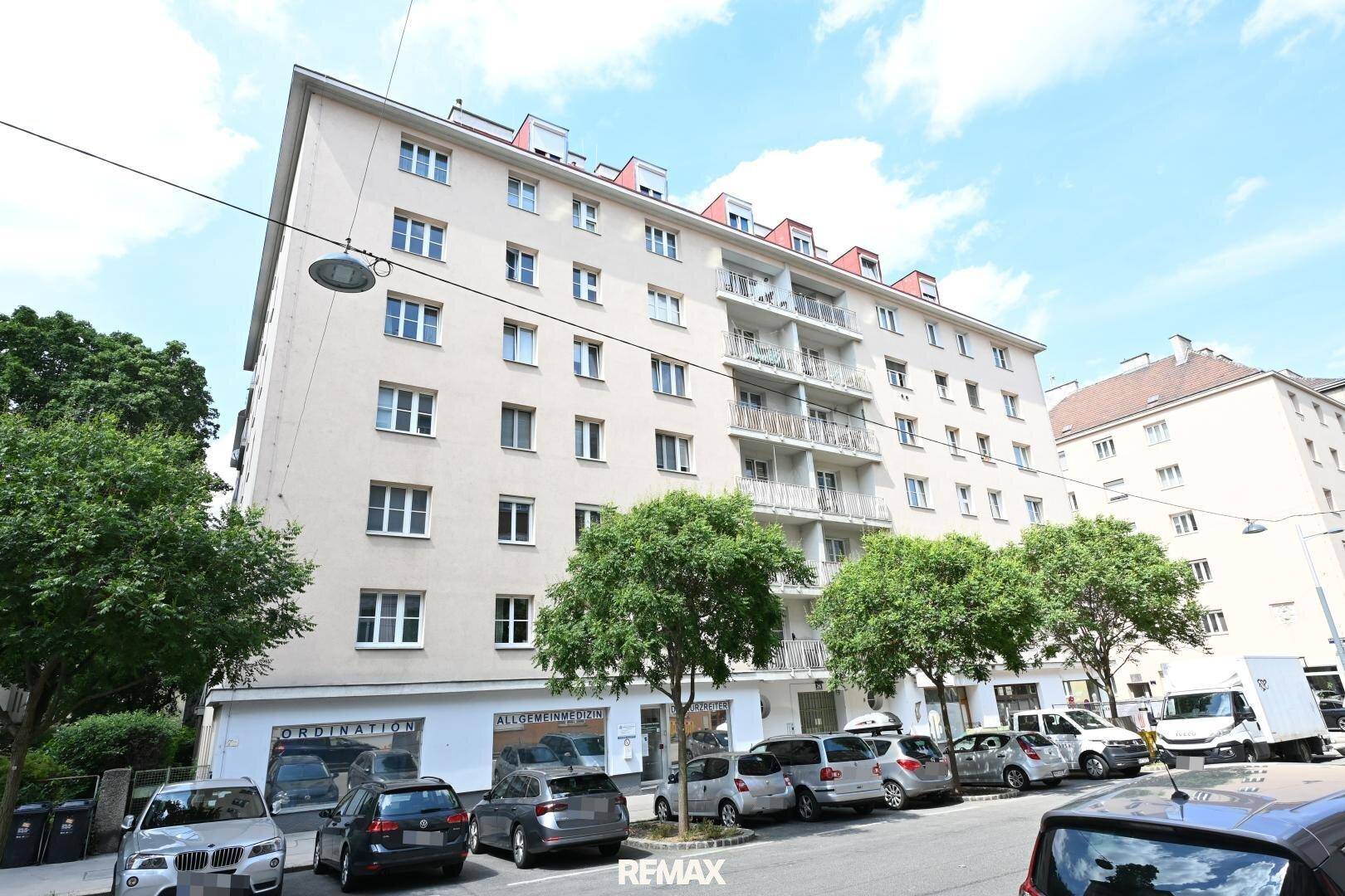Mehrstöckiges Wohngebäude mit Balkonen und Geschäften im Erdgeschoss, an einer belebten Straße gelegen.