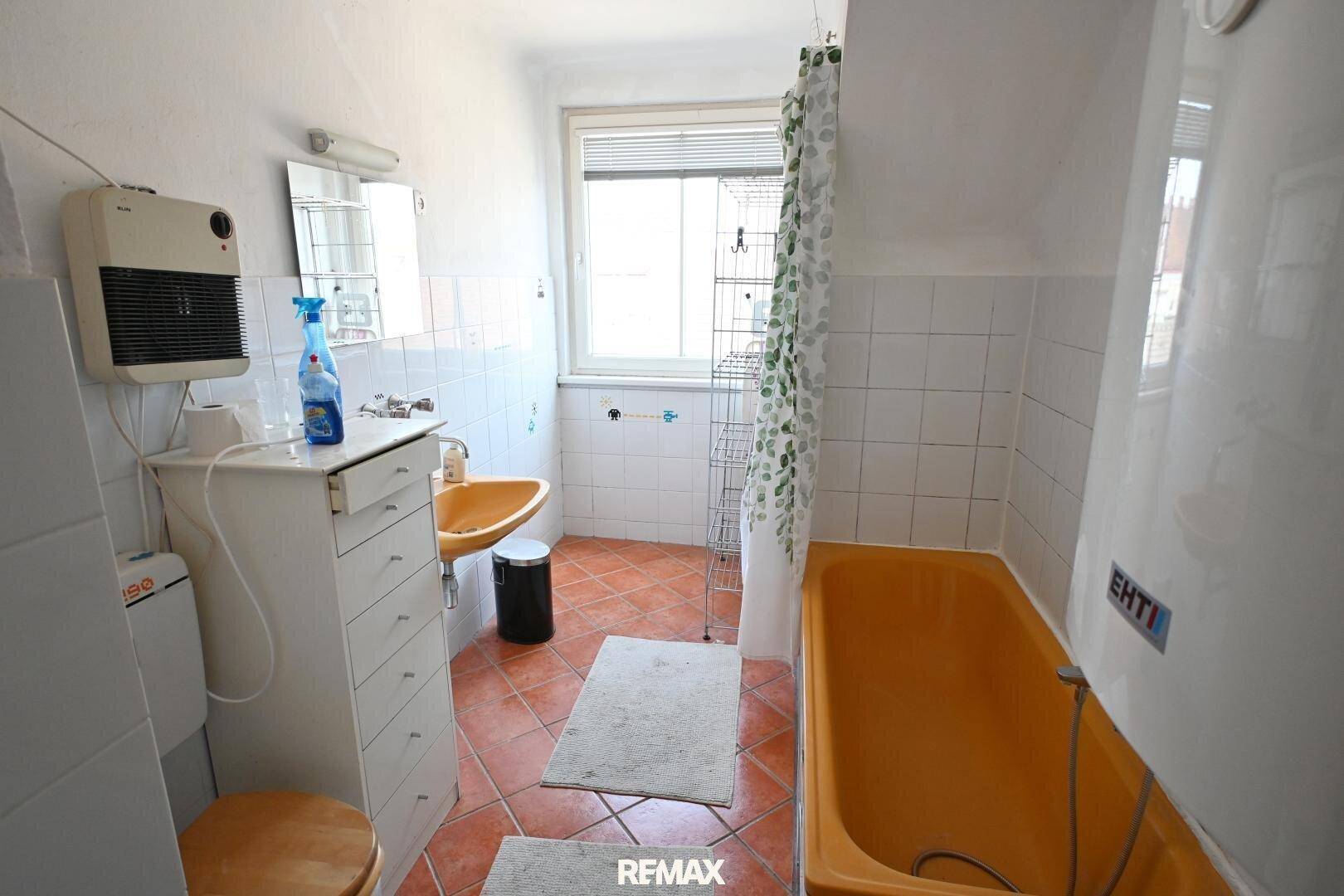 Badezimmer im 80er-Jahre-Stil mit orangefarbener Badewanne und Waschbecken, sowie Terrakotta-Fliesenboden.