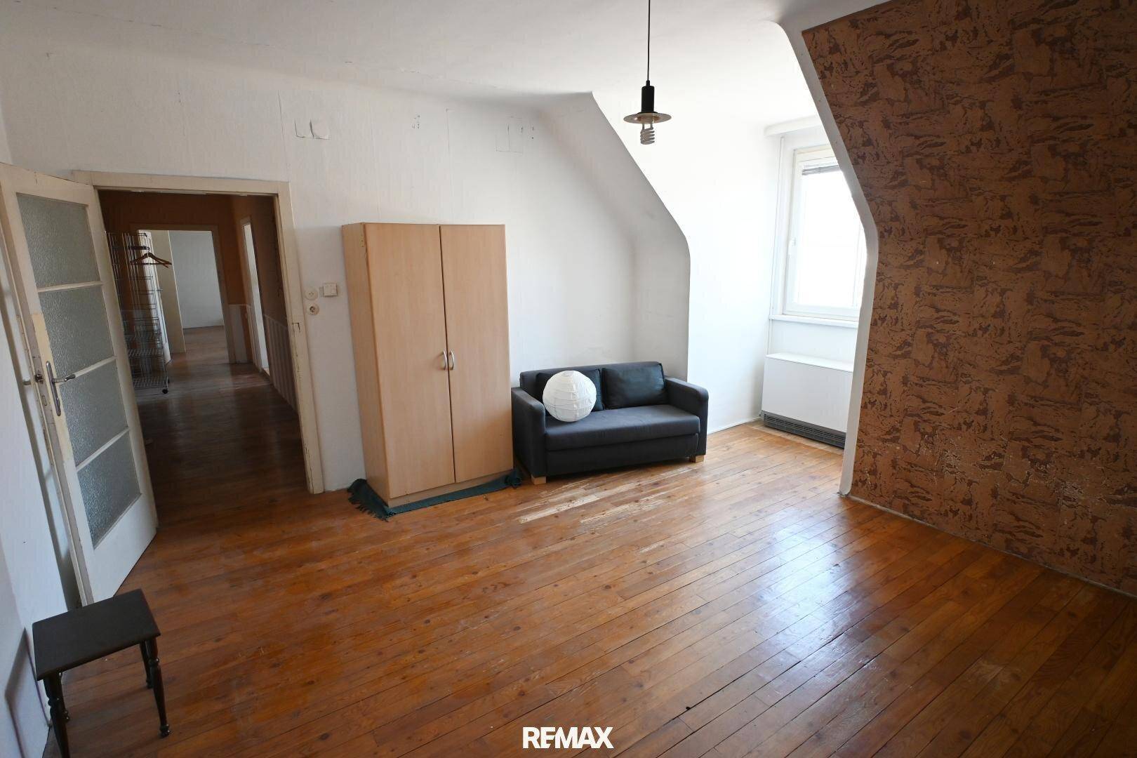 Heller Wohnraum mit Holzdielenboden, Dachschräge und einem kleinen Sofa, ideal für entspannte Stunden.