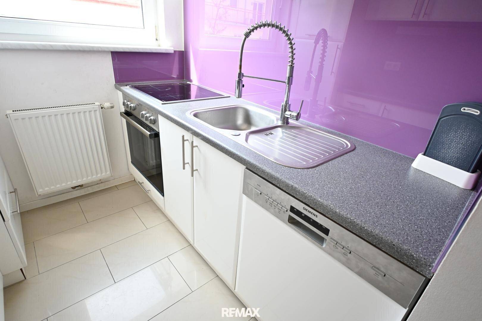 Detailansicht der Küche mit Spüle, Induktionskochfeld, Backofen und integriertem Geschirrspüler.