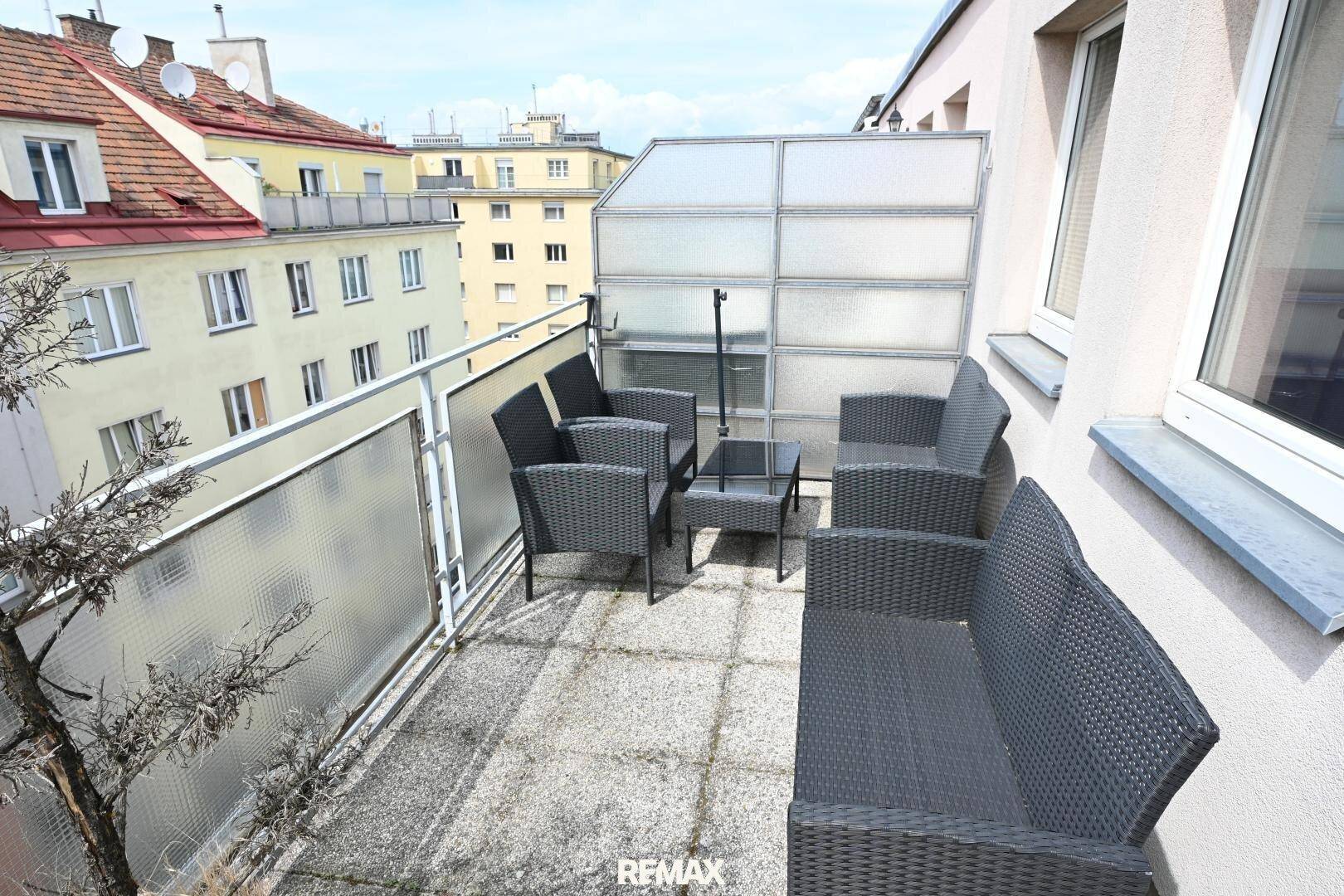 Balkon mit Outdoor-Sitzgruppe und teilweiser Verglasung, bietet einen geschützten Außenbereich.