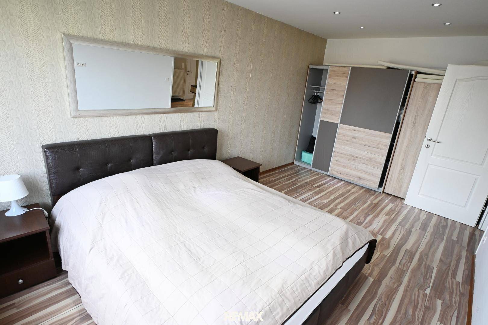Schlafzimmer mit Doppelbett, Nachttisch und großem Kleiderschrank, mit Laminatboden.