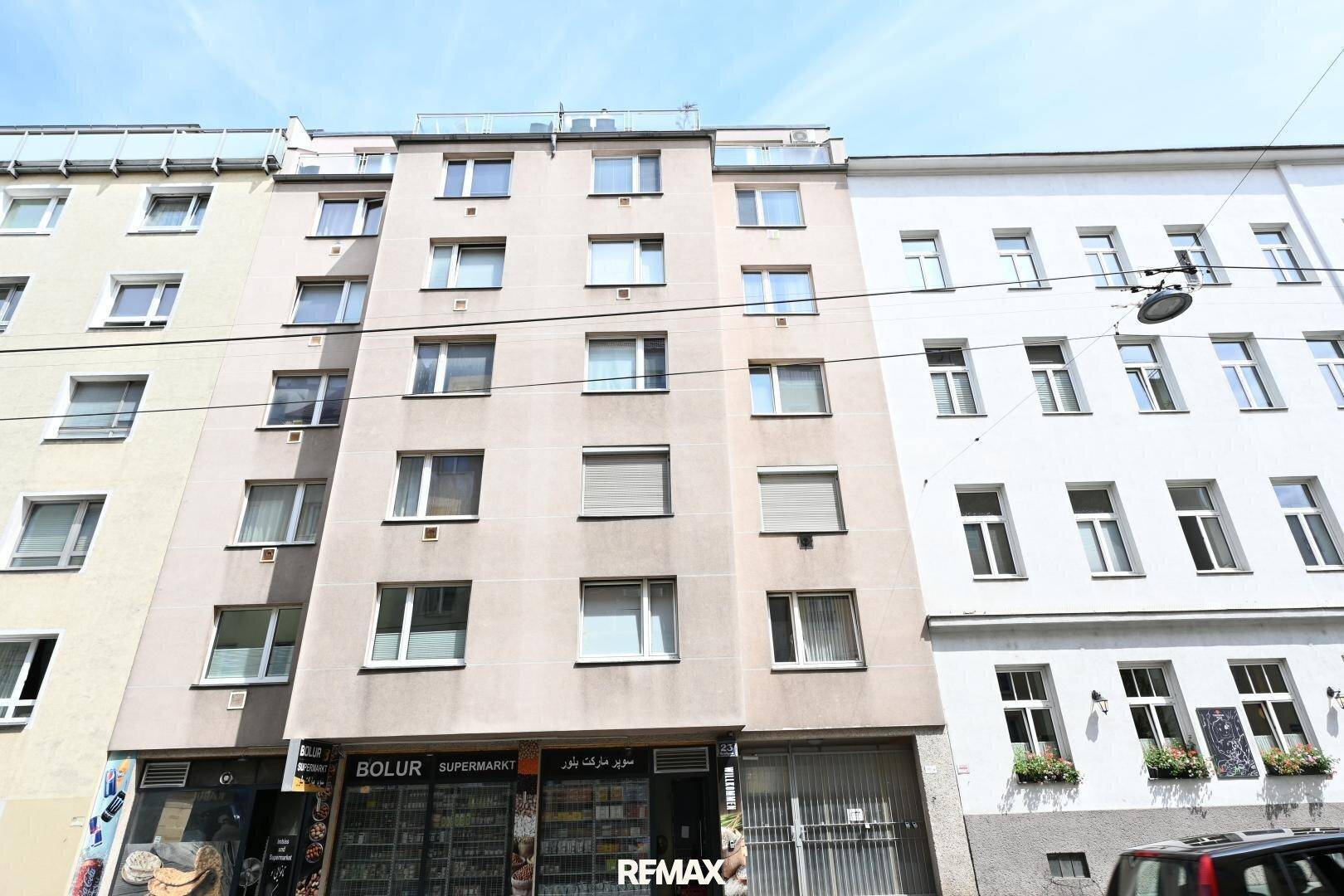 Fassade eines Mehrfamilienhauses mit Geschäften im Erdgeschoss und vielen Fenstern.