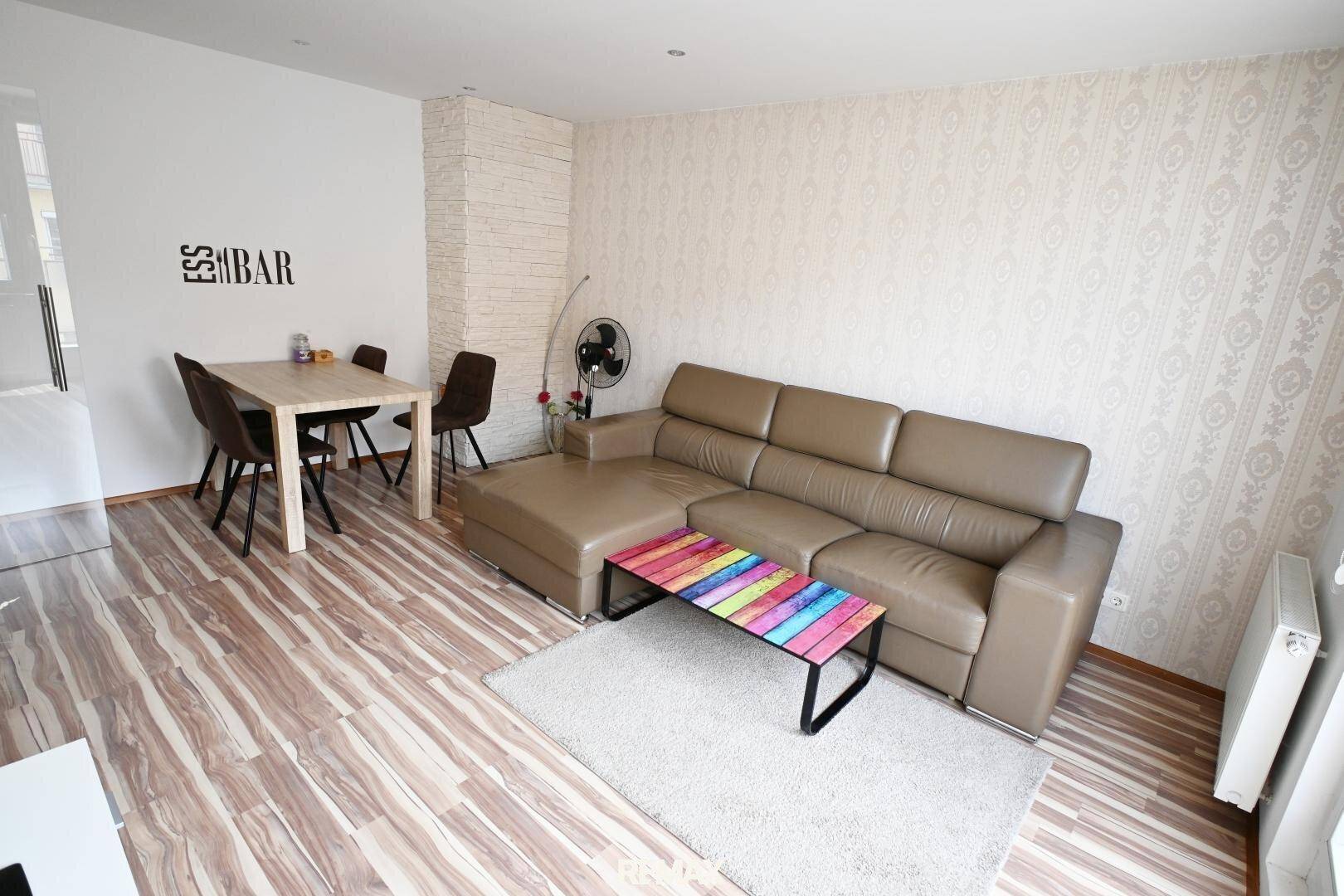 Gemütlicher Wohn-Essbereich mit beigem Sofa, Esstisch und gemusterten Tapeten.