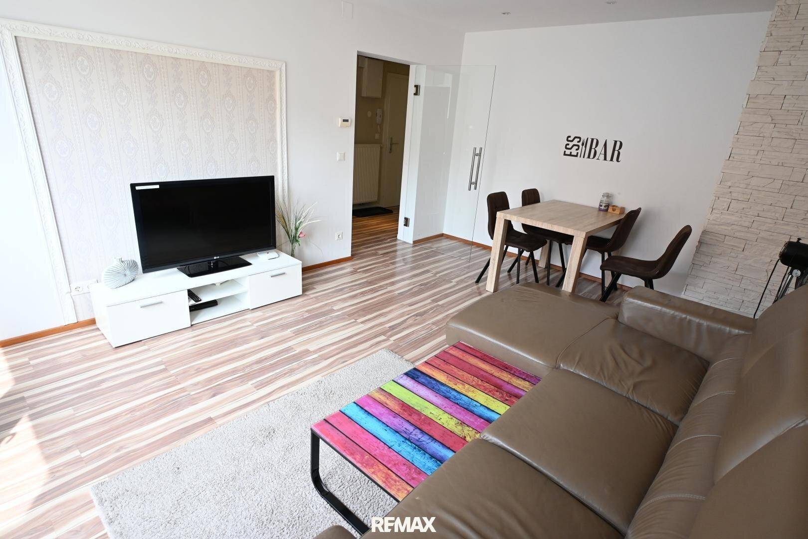 Heller Wohn-Essbereich mit Fernseher, Sofa und Esstisch, durch eine Tür verbunden.