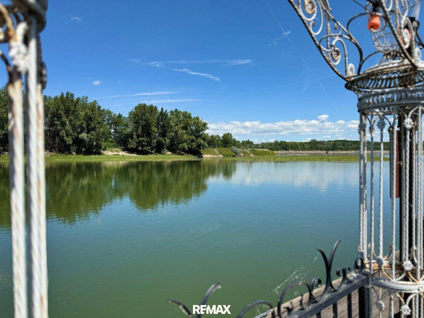 Panoramablick auf den ruhigen See und die bewaldete Uferlandschaft, gerahmt von einem dekorativen Geländer.