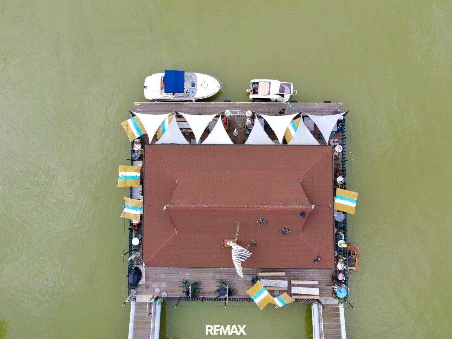 Luftaufnahme direkt von oben auf das schwimmende Gebäude mit Booten und Sonnensegeln auf dem Wasser.