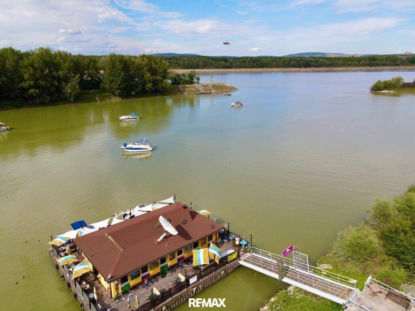 Luftaufnahme des schwimmenden Restaurantkomplexes am Seeufer, umgeben von grüner Natur und weiteren Booten.