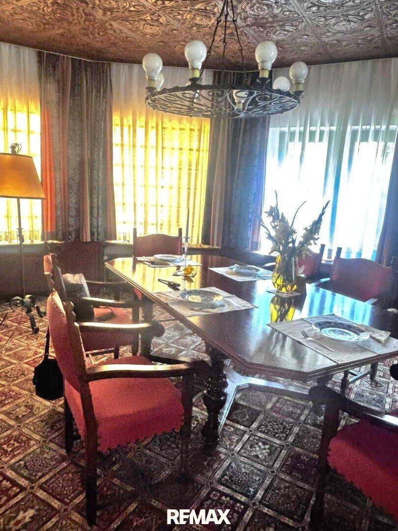 Elegantes Esszimmer mit großem Holztisch, roten Stühlen und dekorativer Decke.