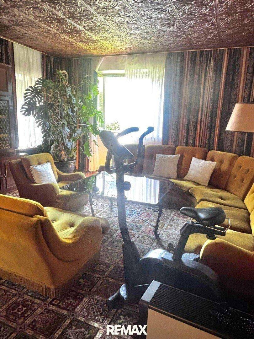 Geräumiges Wohnzimmer mit Fitnessgerät, gemütlichen Sofas und gemusterter Decke.