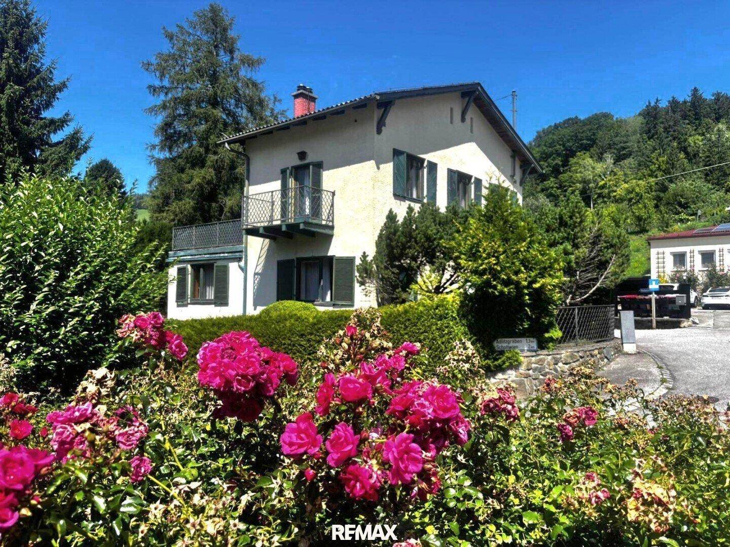 Charmantes Haus mit Balkon und üppigem Rosengarten in einer grünen Umgebung.