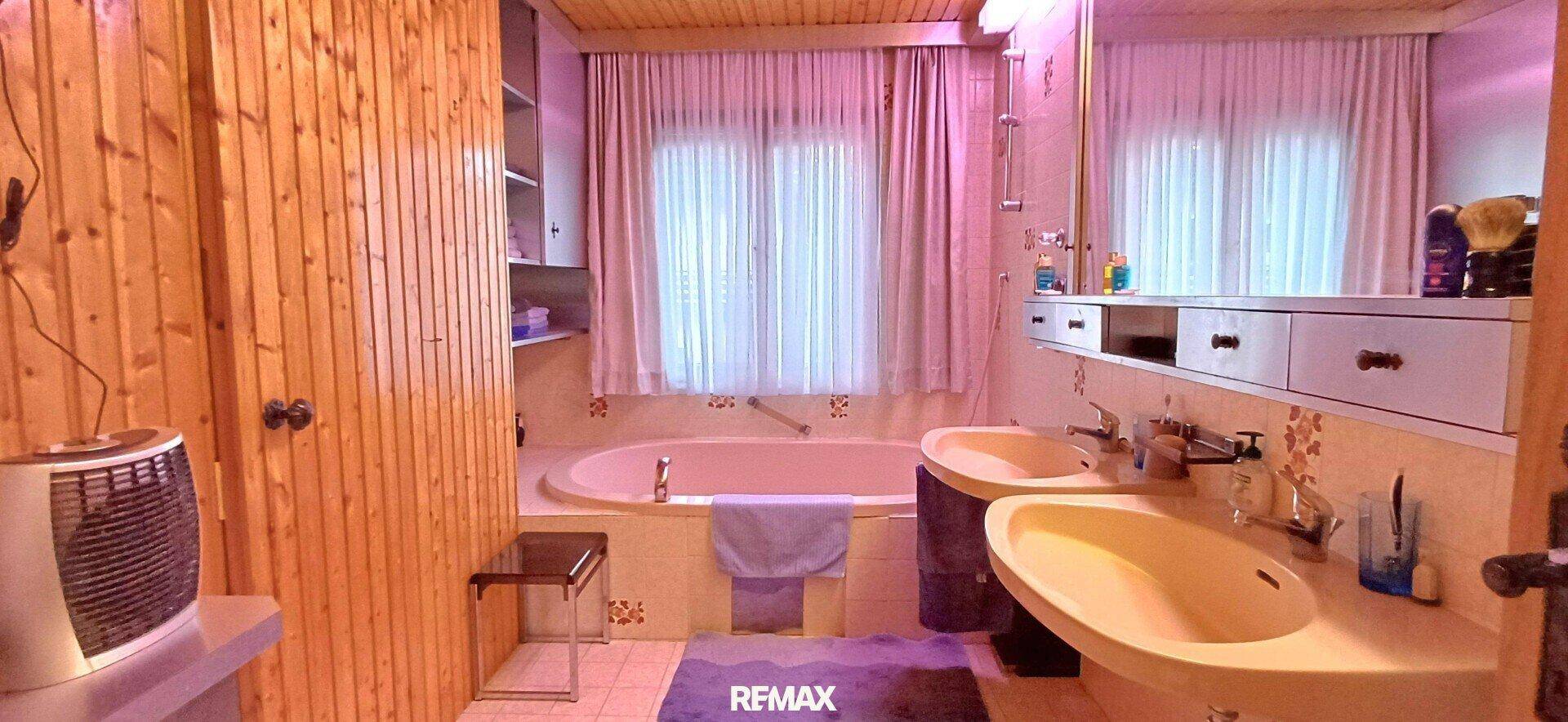 Badezimmer mit Holzverkleidung, zwei Waschbecken und einer Badewanne.