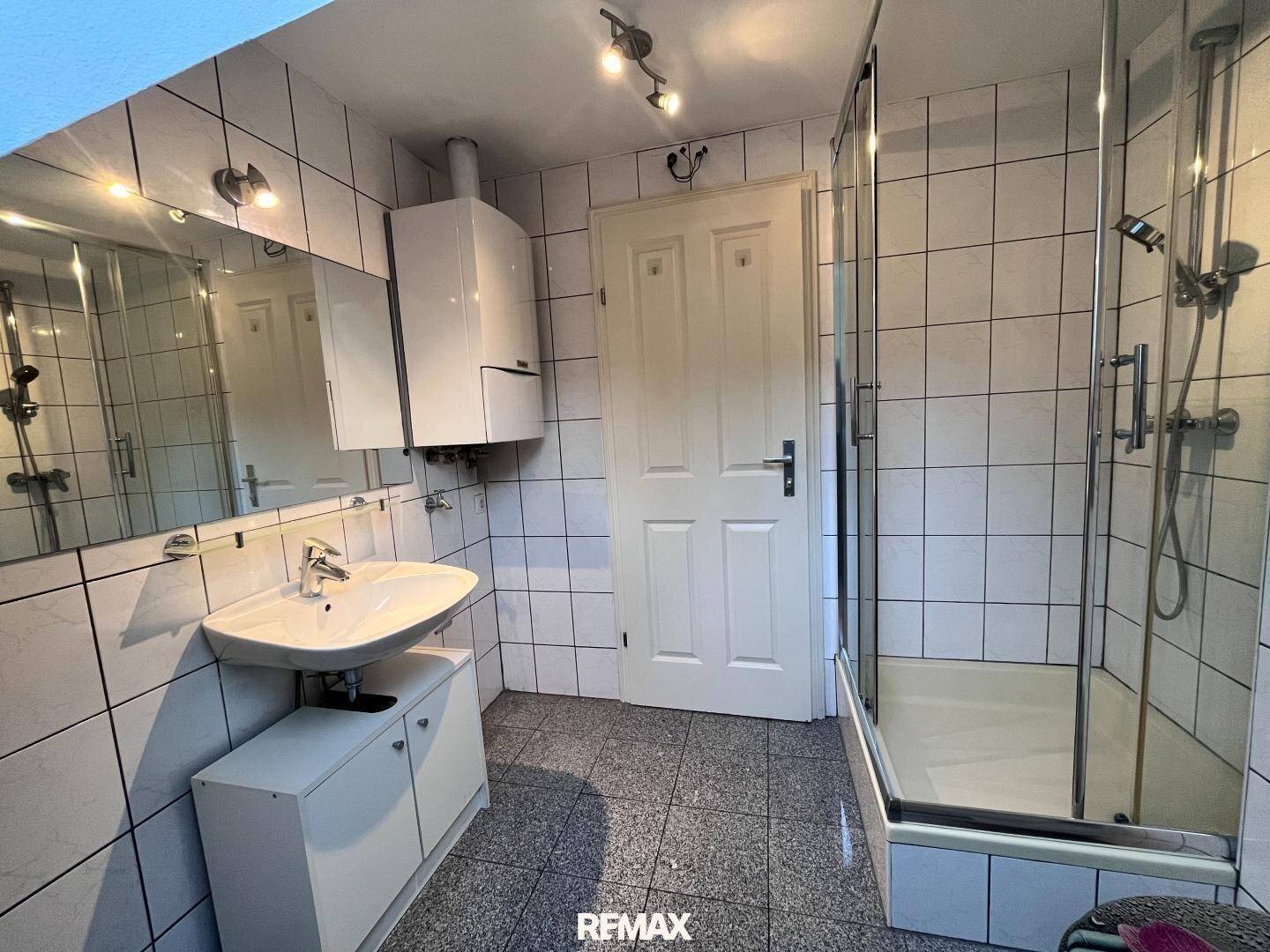 Gefliestes Badezimmer mit Dusche, Waschbecken und Spiegelschrank in hellen Farben.