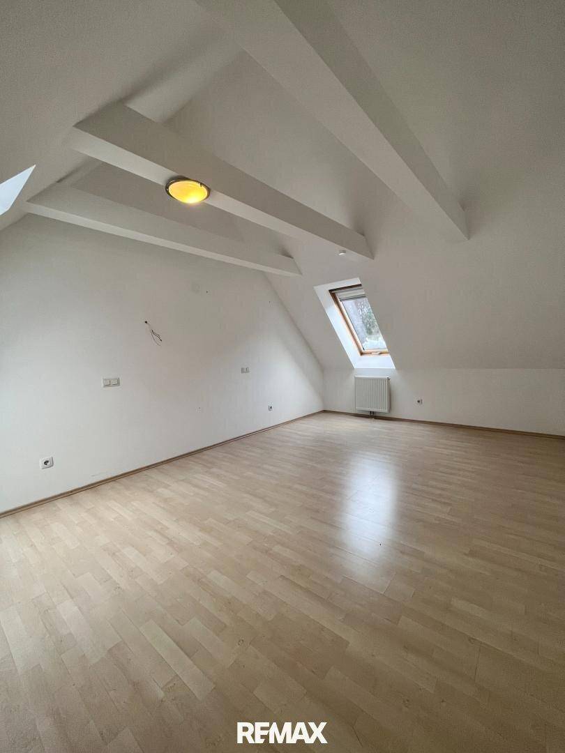 Helles Zimmer im Dachgeschoss mit Holzboden, Dachschräge und einem Dachfenster.