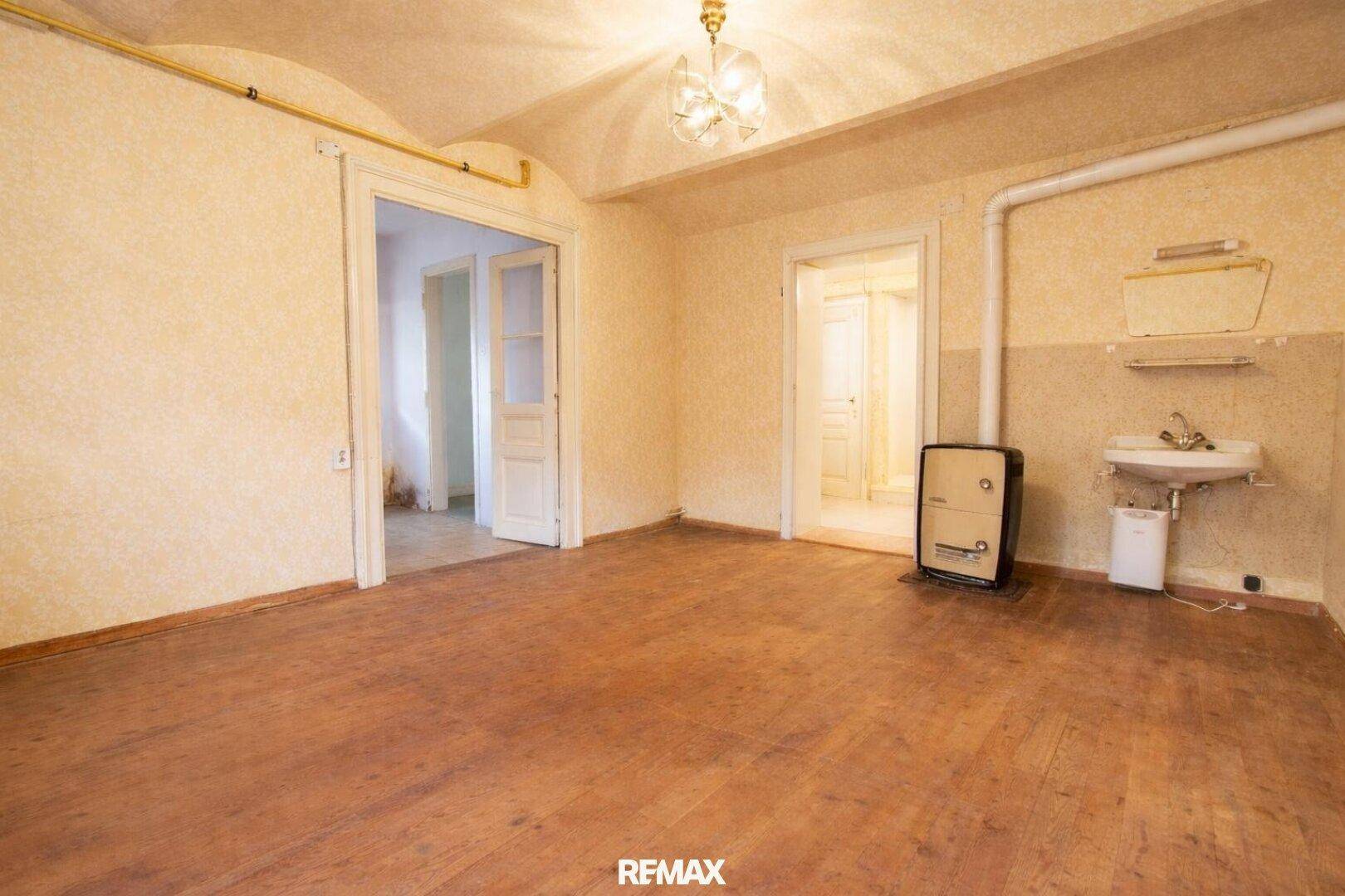 Unmöbliertes Wohnzimmer mit Holzboden, hohen Decken und einem alten Ofen, bereit zur Renovierung.