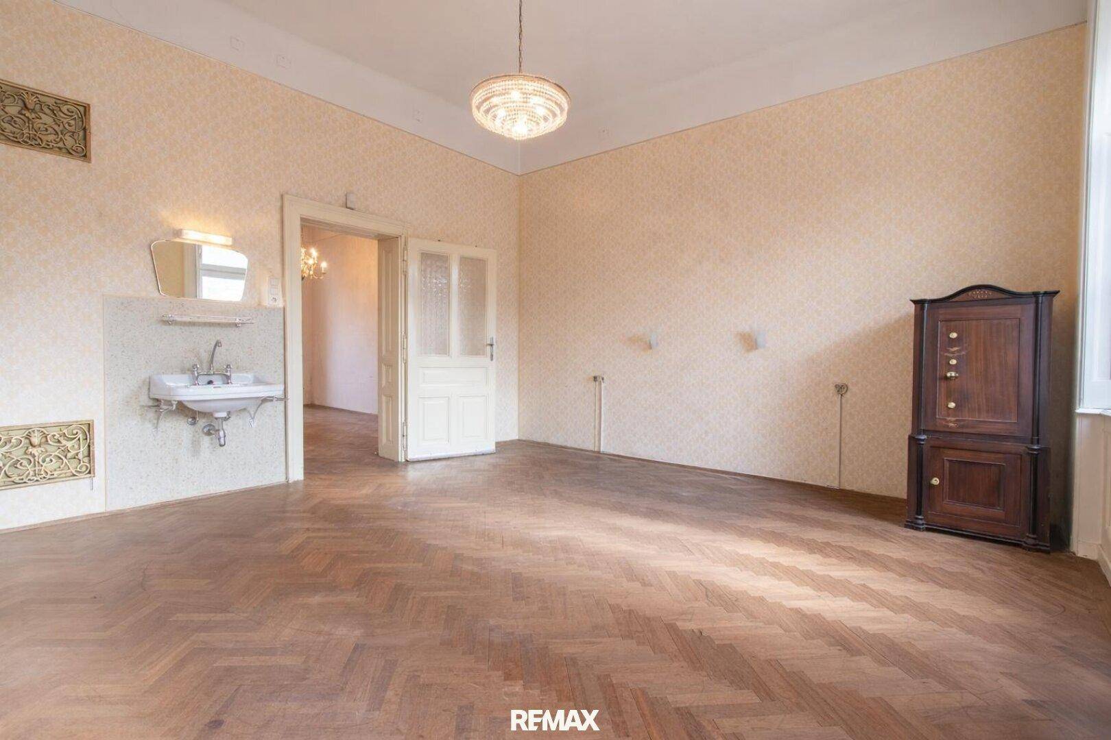 Geräumiges Schlafzimmer mit Fischgrätparkett, Stuckdecke und einem Waschbecken, in originalem Zustand.