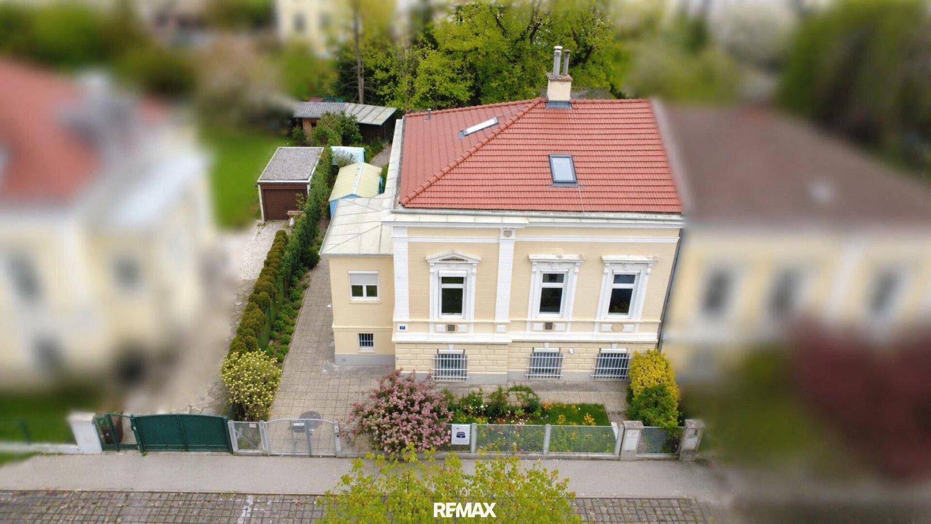Luftaufnahme eines charmanten gelben Hauses mit rotem Ziegeldach und gepflegtem Gartenbereich.
