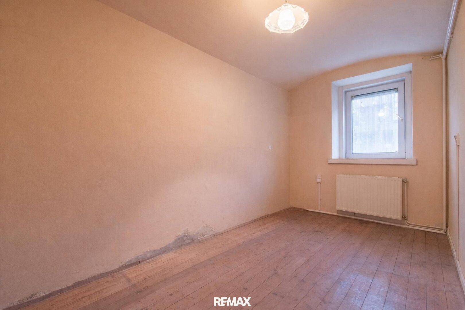 Unmöbliertes Zimmer mit hellbraunen Wänden, Holzboden und einem Fenster, in originalem Zustand.