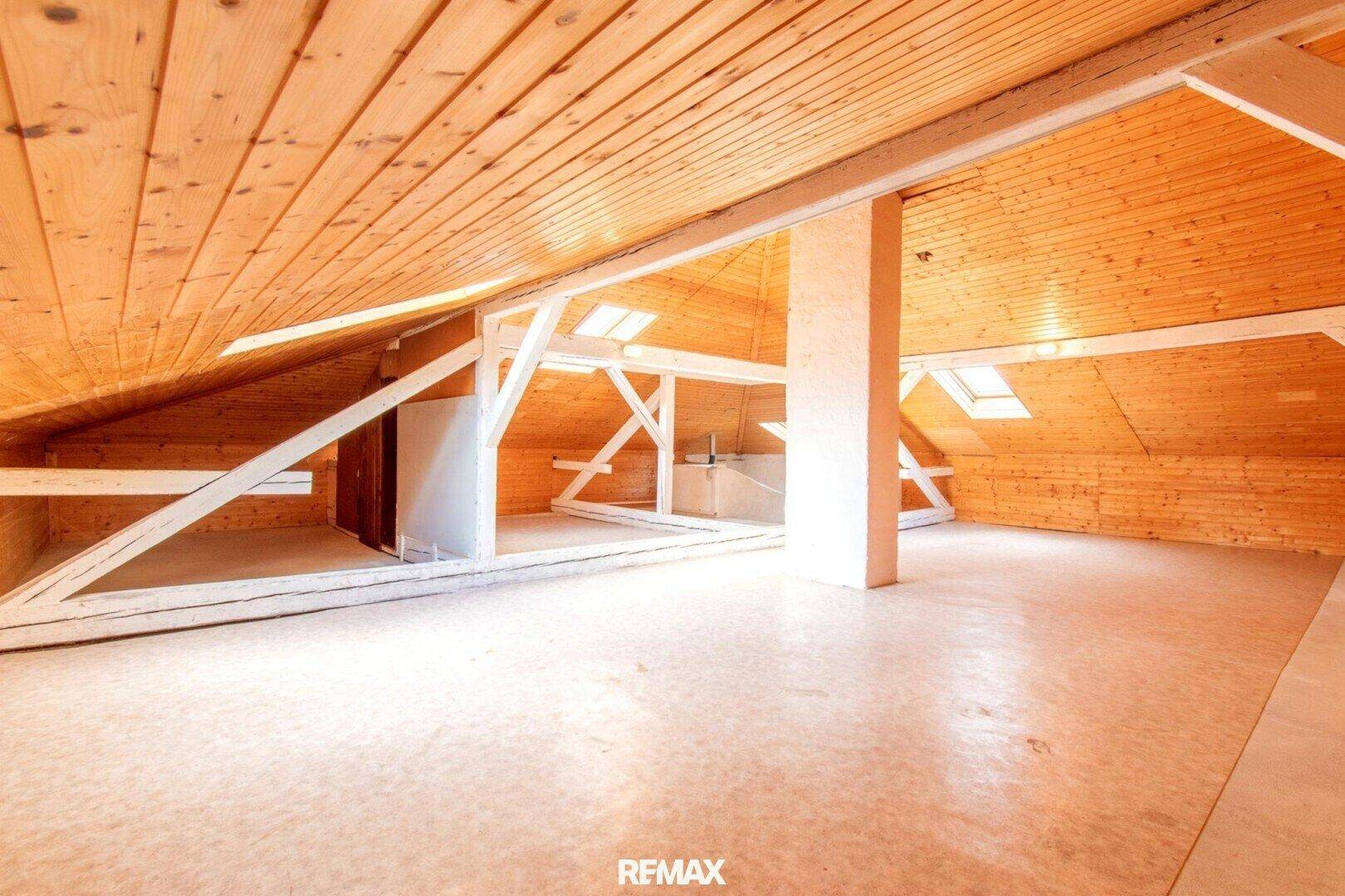 Ausgebauter Dachboden mit Holzverkleidung, sichtbaren Balken und Dachfenstern, hell und geräumig.