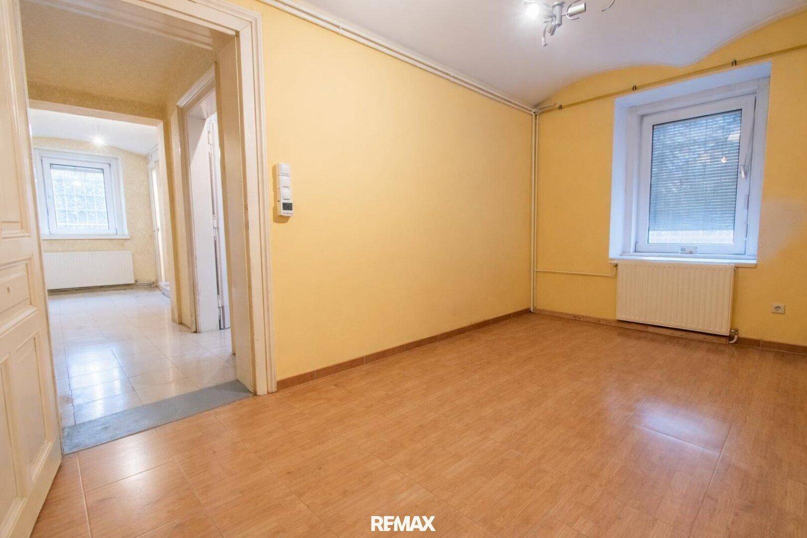 Leeres Schlafzimmer mit gelben Wänden, Laminatboden und einem Fenster mit Heizkörper darunter.
