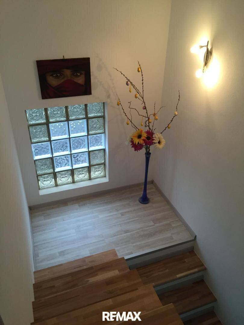 Treppenhaus mit Holzstufen, Glasbausteinwand und Wandleuchte.