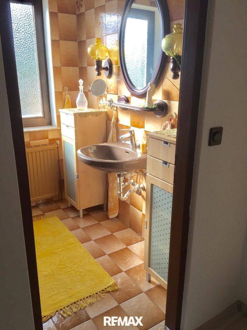 Badezimmer mit braunen Fliesen, Waschbecken und Spiegelschrank im 80er-Jahre-Stil.