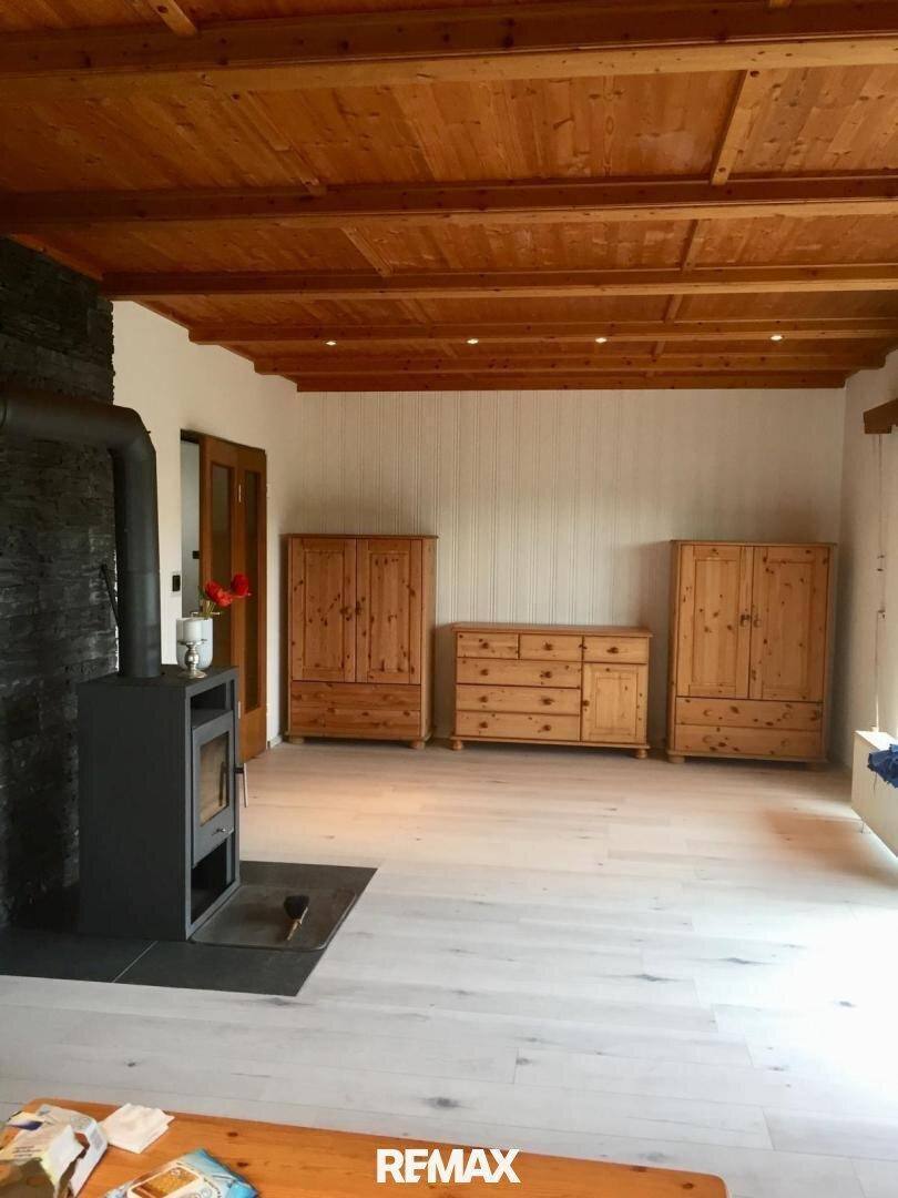 Geräumiges Wohnzimmer mit Holzbalkendecke, Kaminofen und hellem Boden.