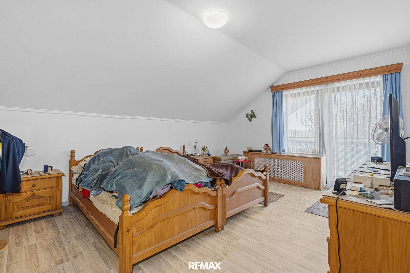 Schlafzimmer im Dachgeschoss mit Holzbett, Dachschräge und Fenster mit Ausblick.