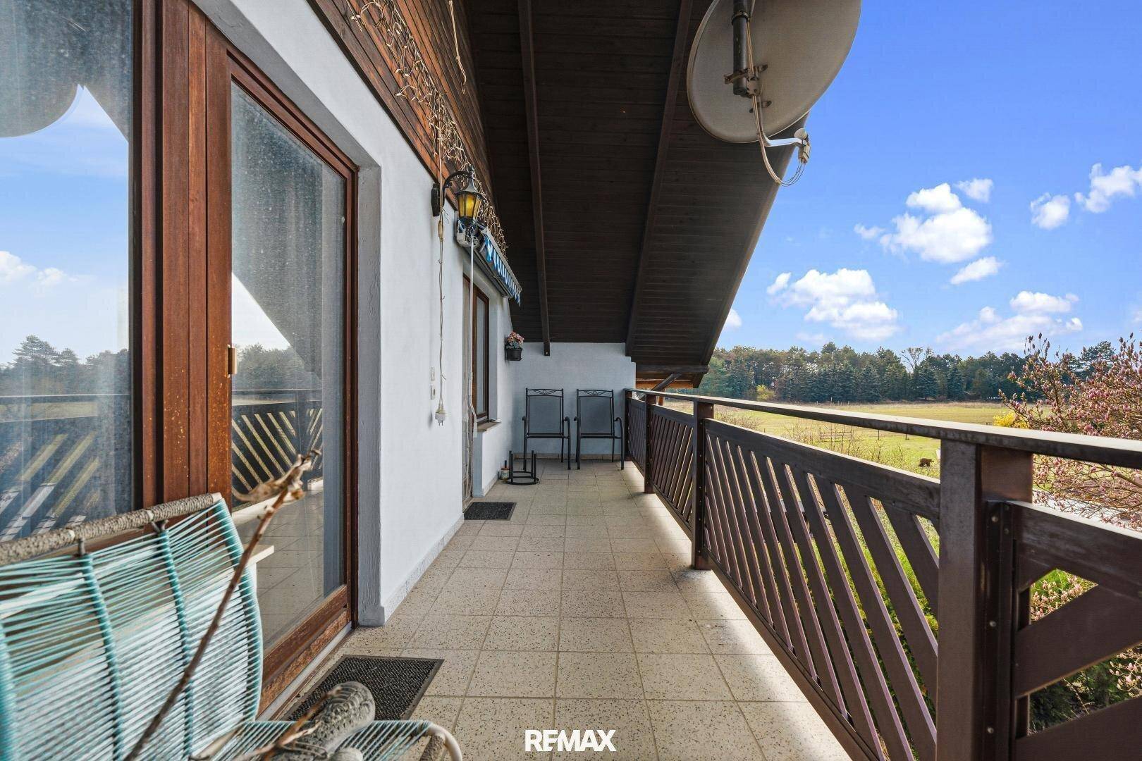 Geräumiger Balkon mit Fliesenboden, Holzgeländer und weitem Blick ins Grüne.