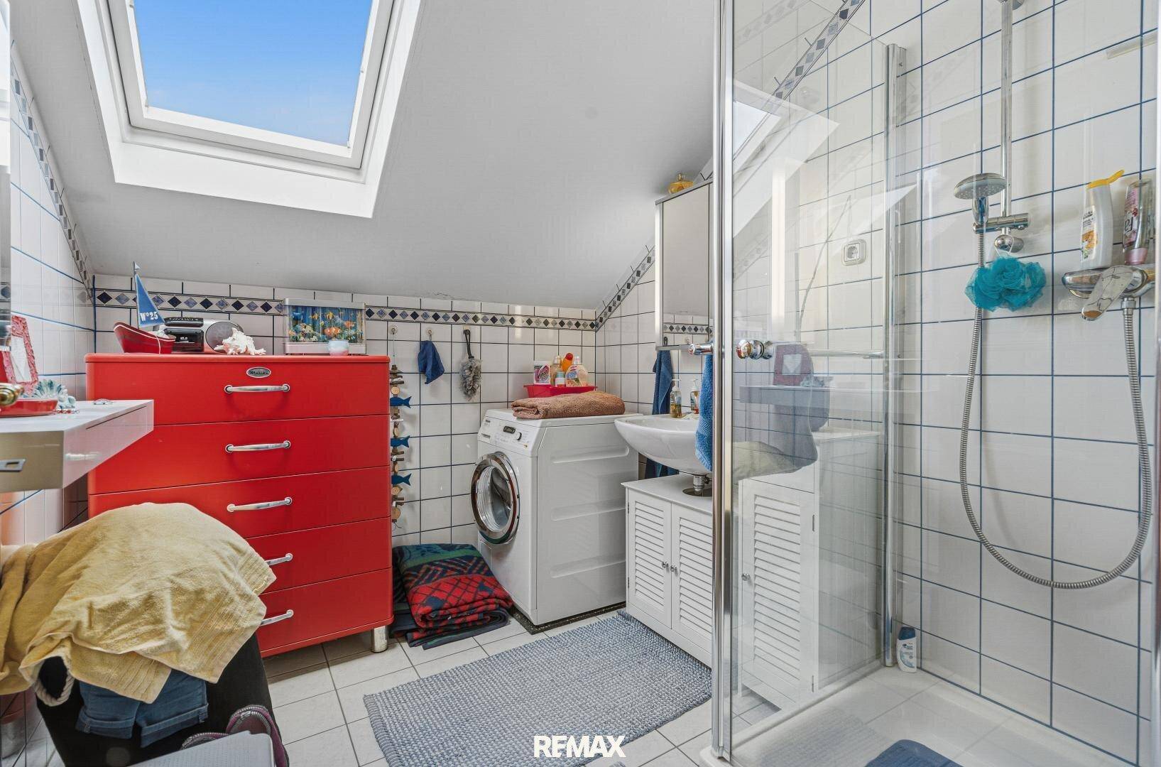 Badezimmer im Dachgeschoss mit Dusche, Waschmaschine und Dachfenster.