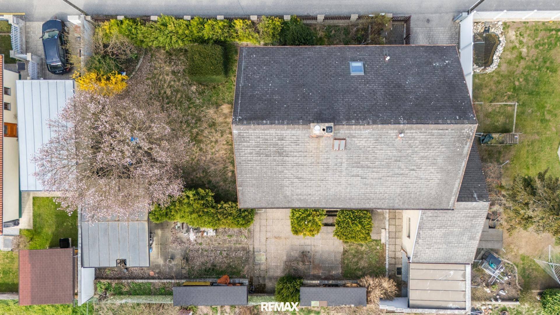 Draufsicht auf das Haus mit Garten, Terrasse und blühendem Baum im Frühling.