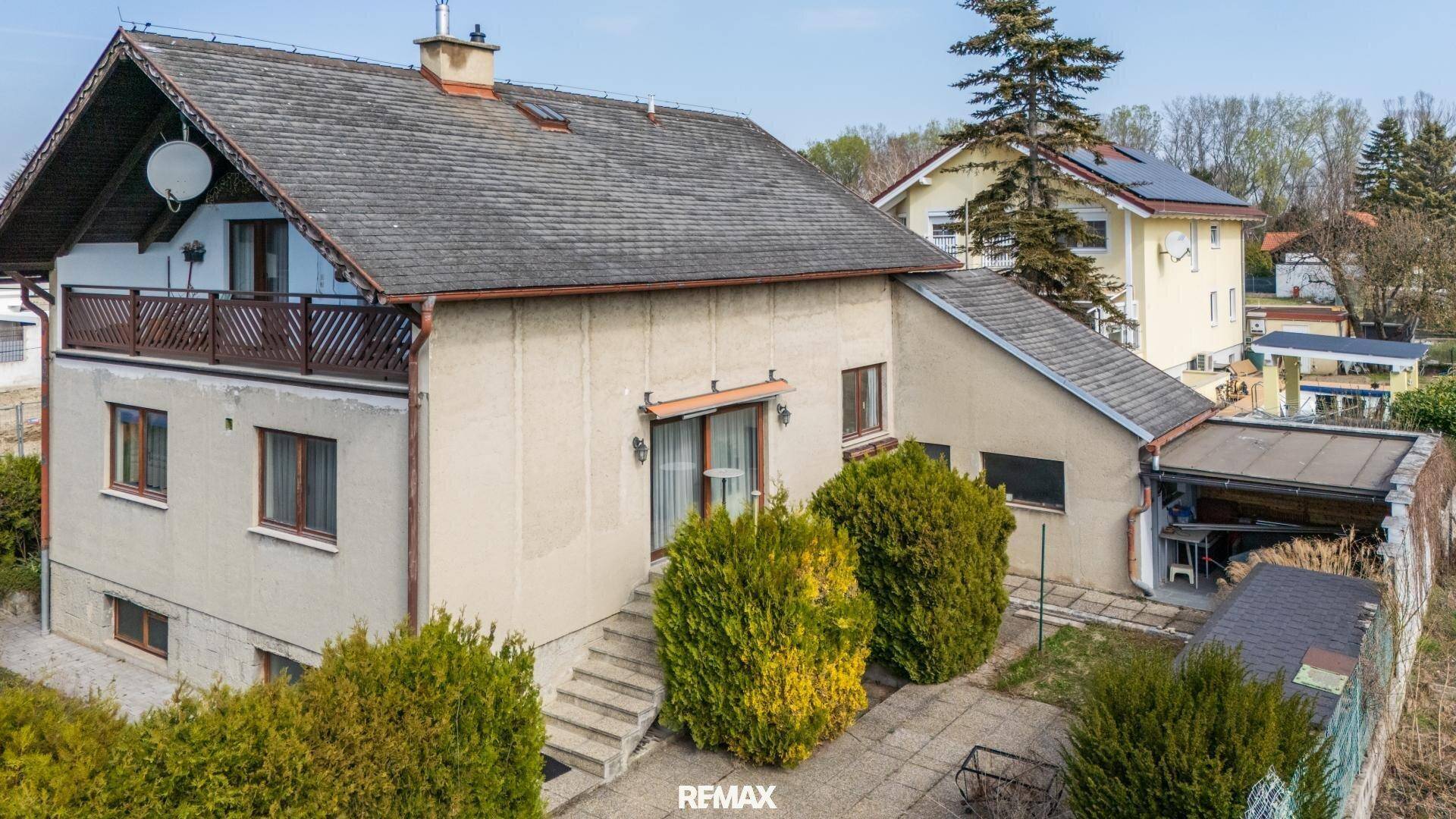 Seitenansicht des Hauses mit Terrasse, Treppe zum Garten und gepflegten Büschen.