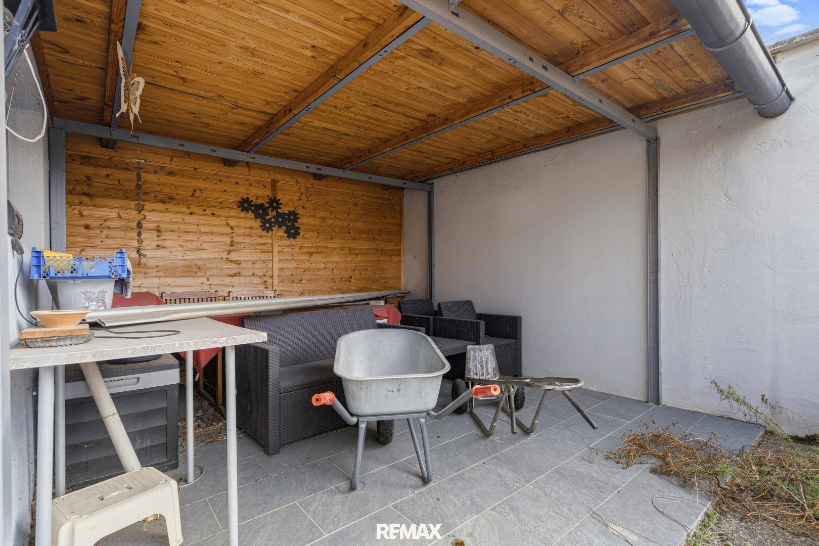 Überdachte Terrasse mit Sitzgelegenheiten und Holzwand.