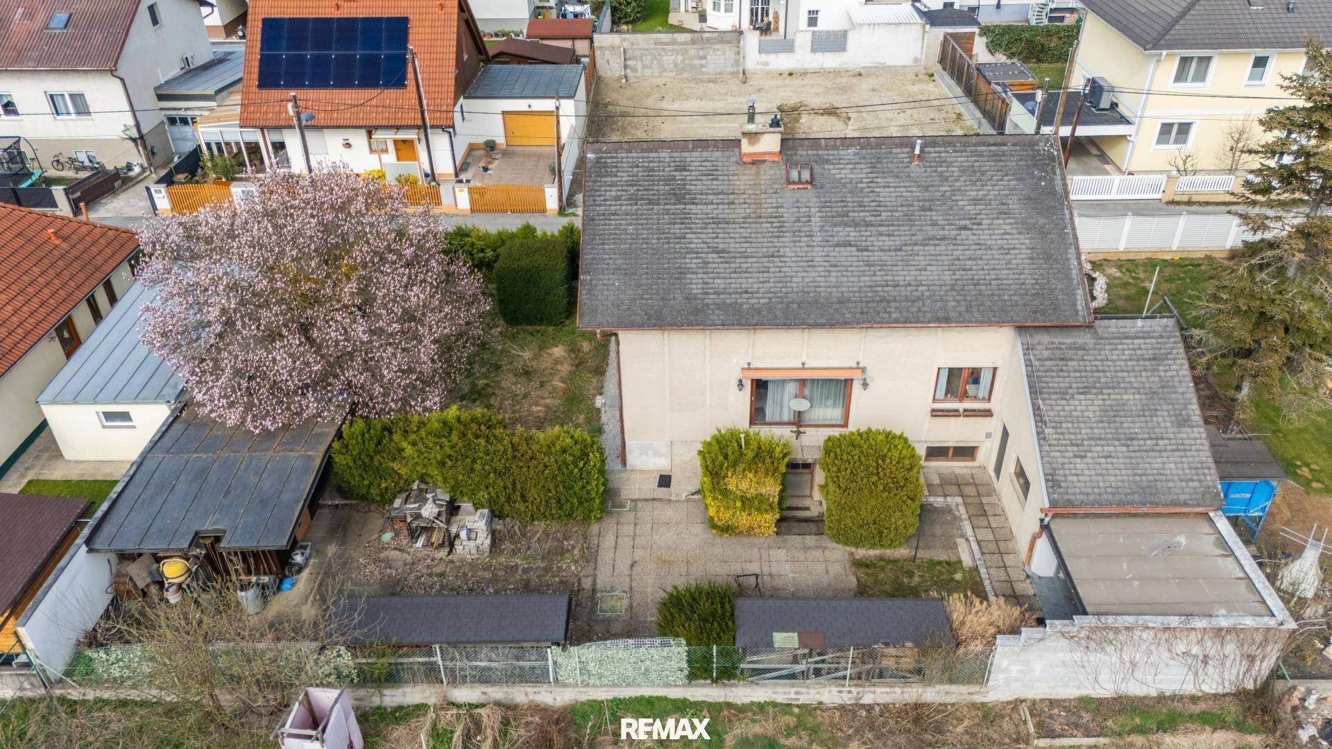 Luftaufnahme eines Einfamilienhauses mit Garten, Terrasse und umliegenden Gebäuden.