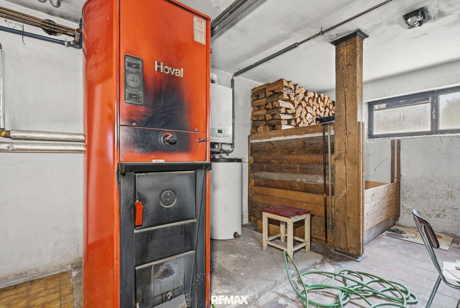 Heizraum im Keller mit großem Heizkessel und Holzstapel.