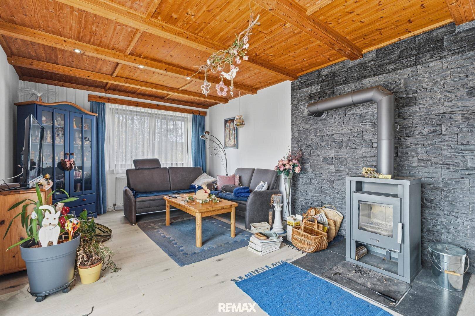 Gemütliches Wohnzimmer mit Holzbalkendecke, Kaminofen und dekorativer Steinwand.