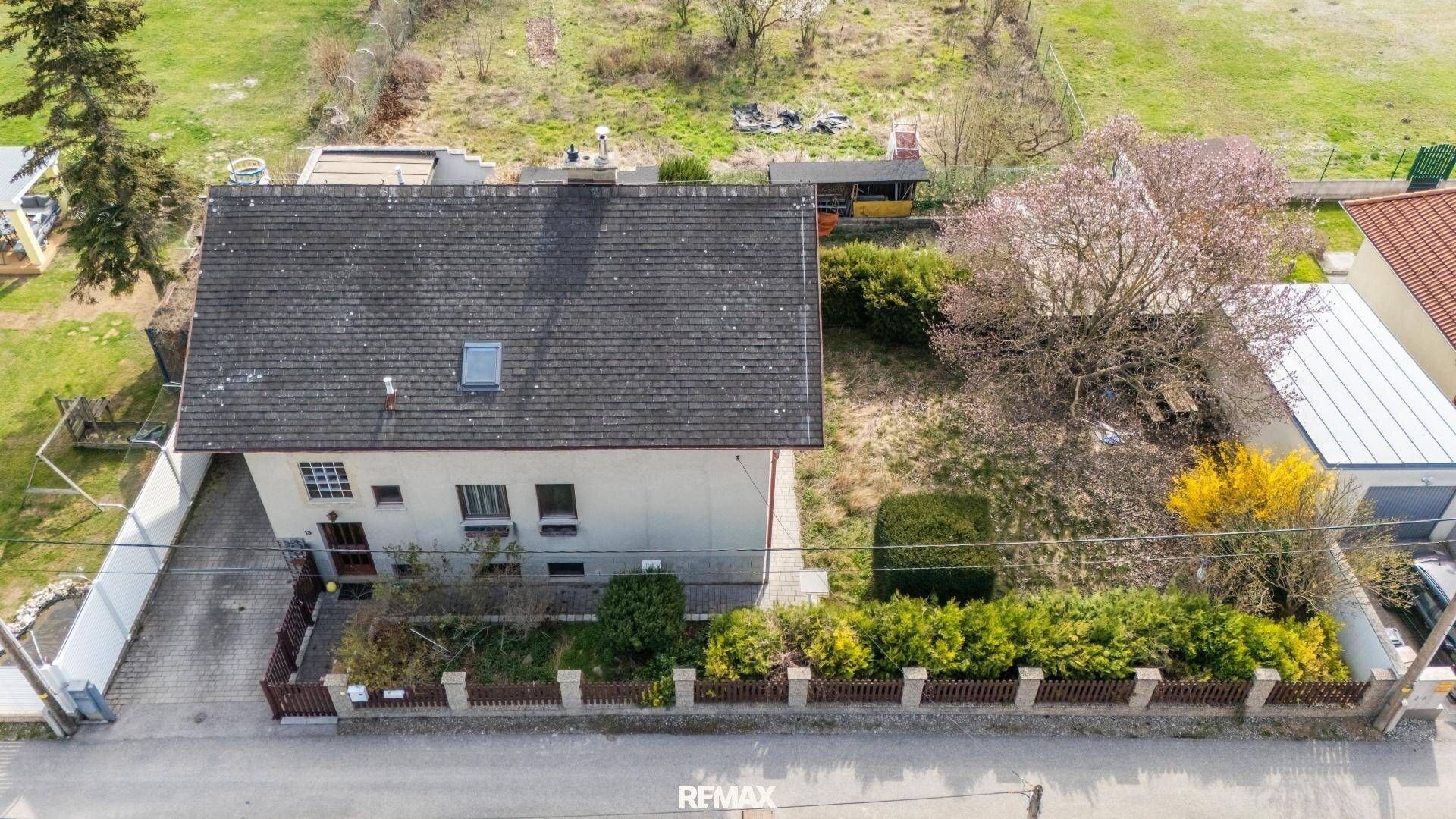 Luftaufnahme der Vorderseite des Hauses mit Vorgarten, Zaun und Zufahrt zur Straße.