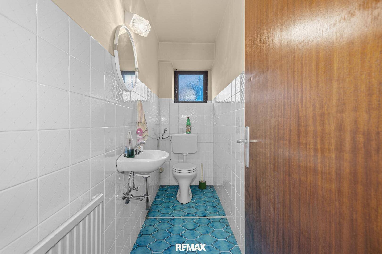 WC mit Waschbecken, Toilette, Fenster und blauen Bodenfliesen.