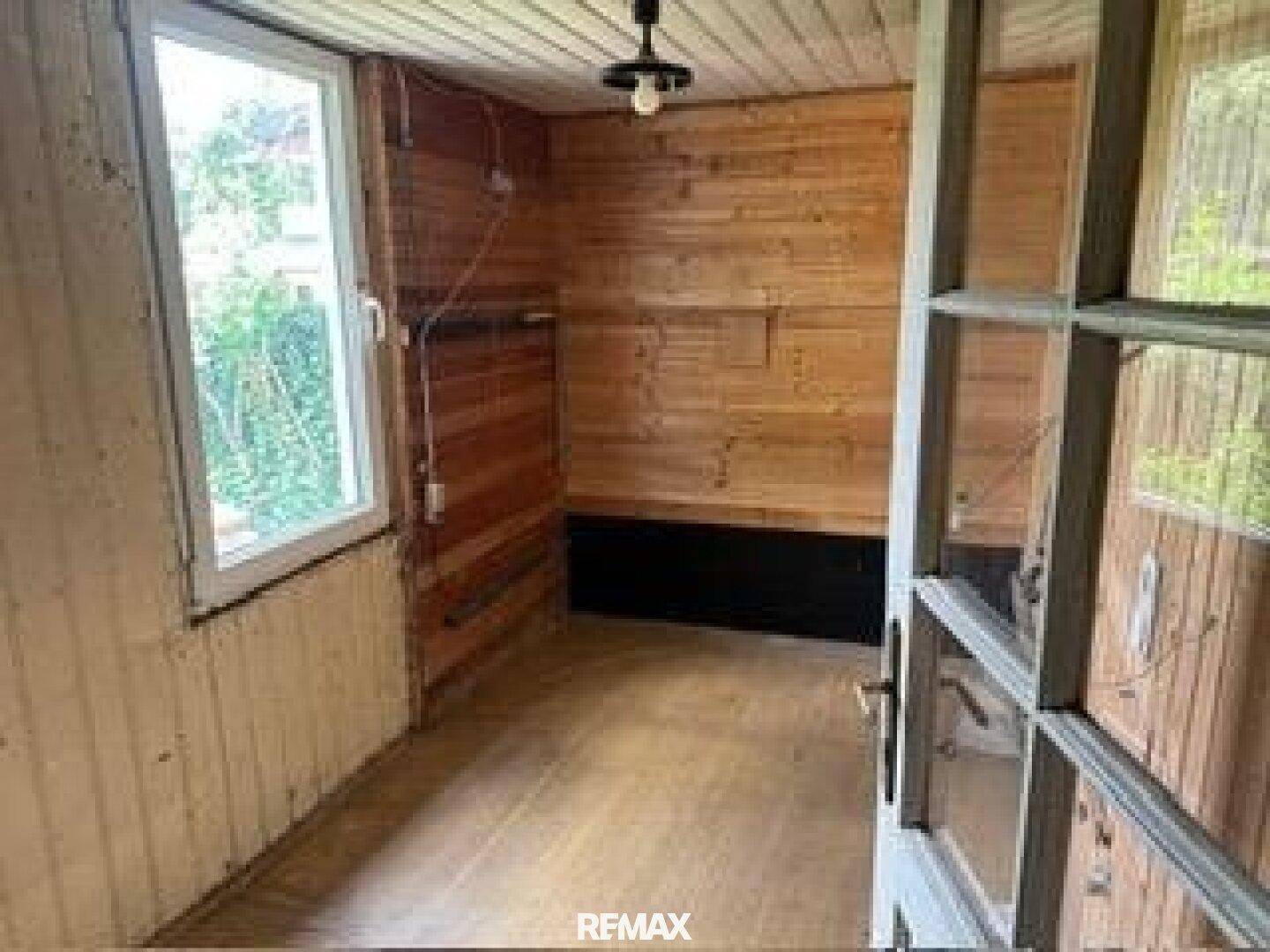 Raum mit Holzvertäfelung, Fenster und Holzboden, möglicherweise ein Wintergarten oder eine Veranda.