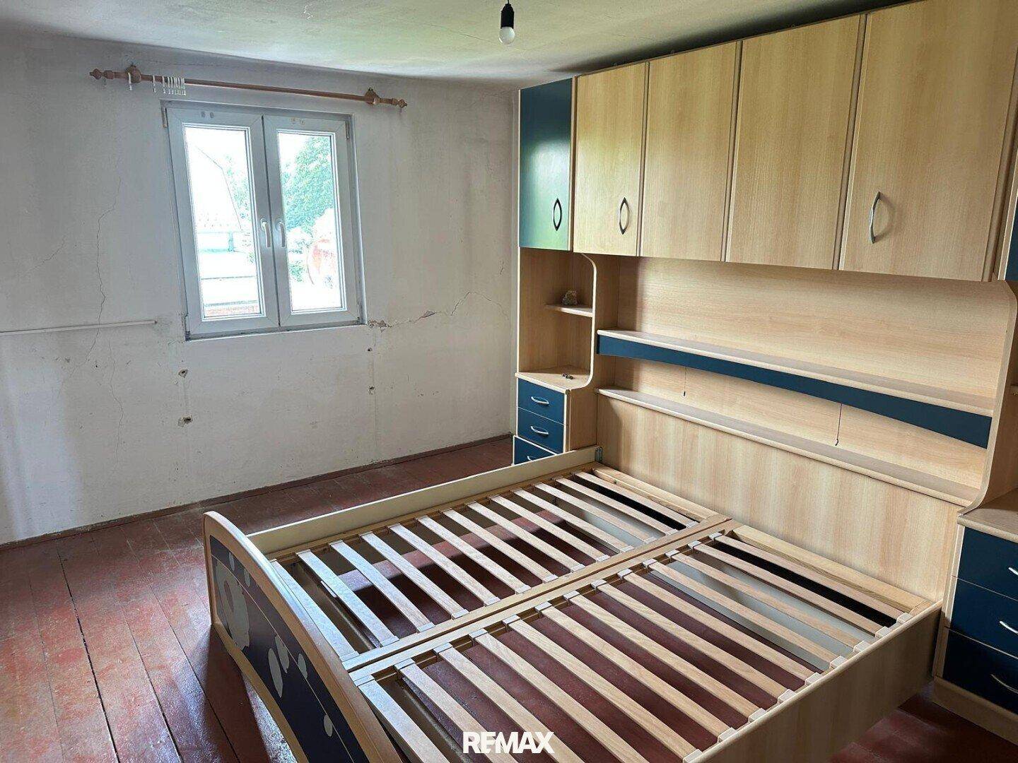 Schlafzimmer mit Bettrahmen und eingebauten Schränken, die Wände zeigen Renovierungsbedarf.