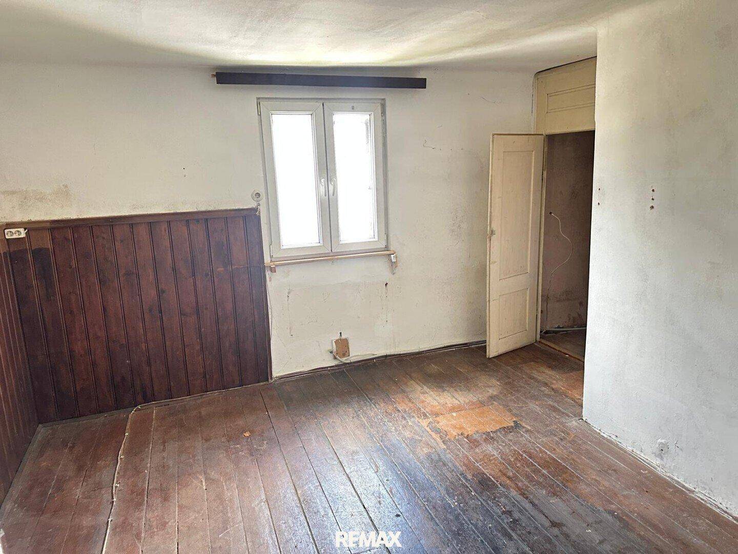 Leeres Zimmer mit Holzdielenboden und Holzvertäfelung an einer Wand, das Renovierung erfordert.